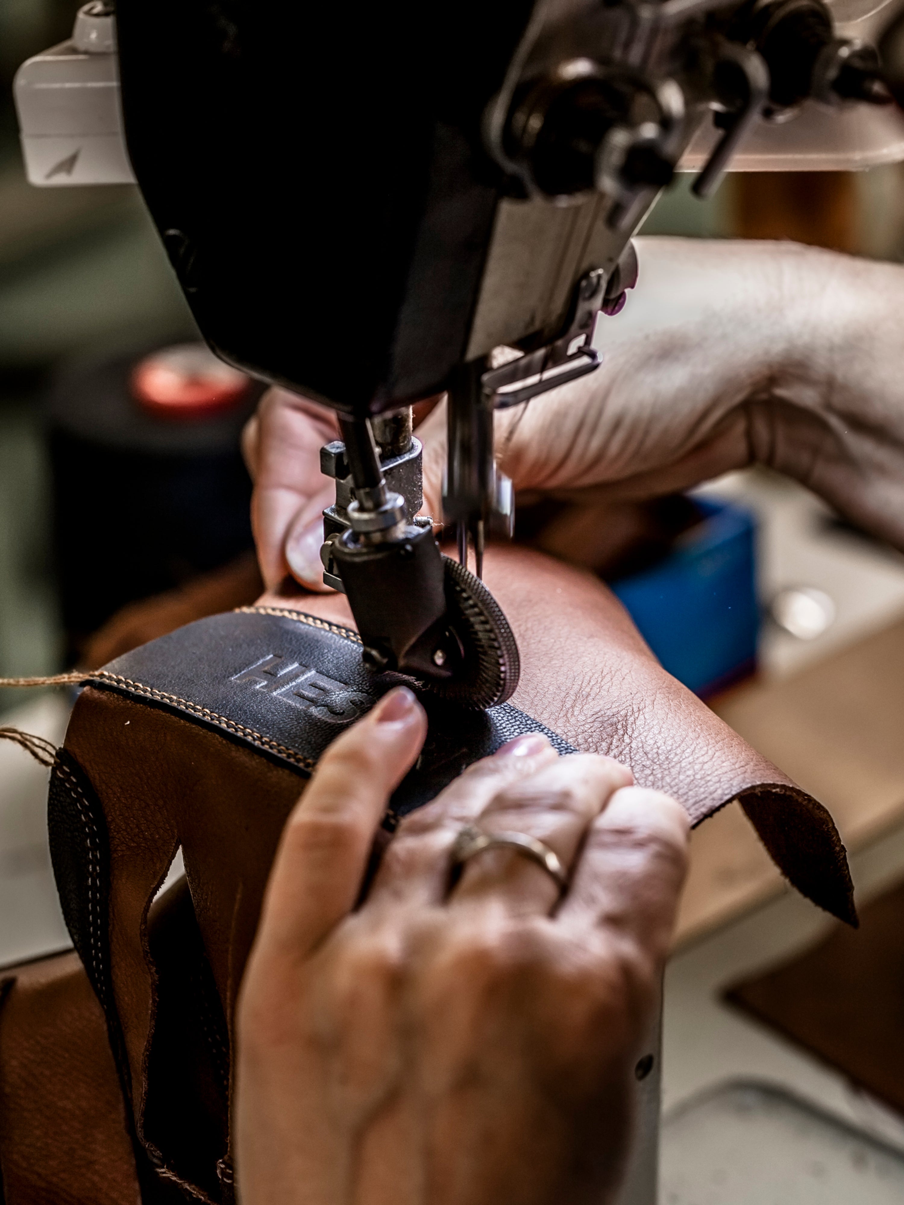 Närbild: händer som syr Hestra-logotypen på ett handskskaft i industrisymaskin